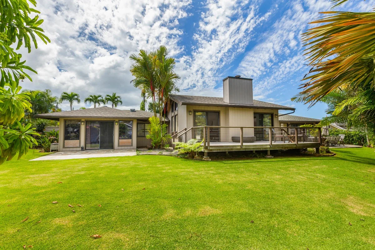 A low-rise house with a raised deck stands beyond a broad green lawn.