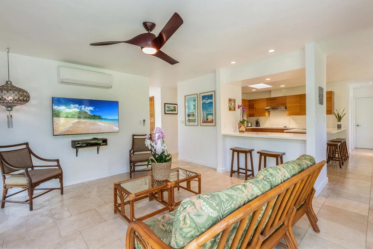 A bright living room with rattan seating, a coffee table, and an open kitchen.