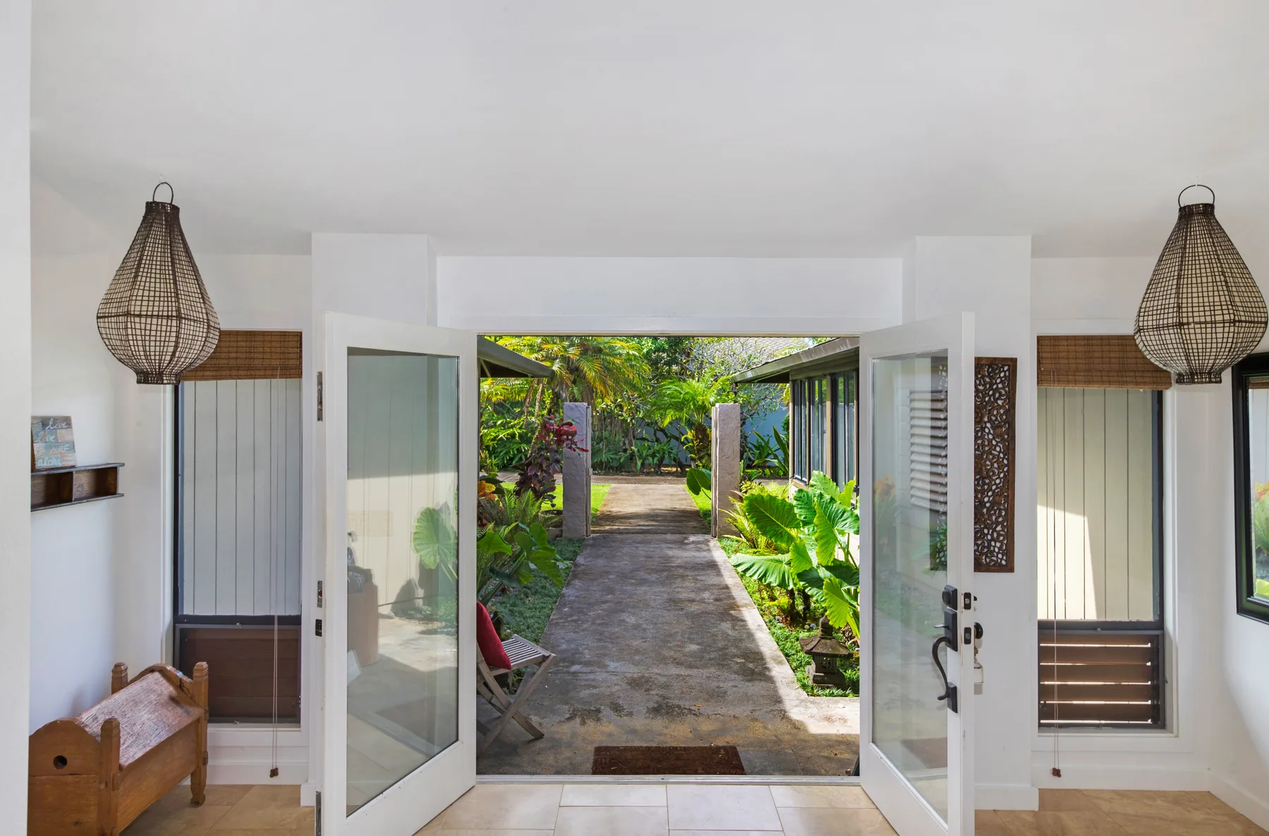 An open doorway leads from a bright interior to a garden path lined with tropical plants.
