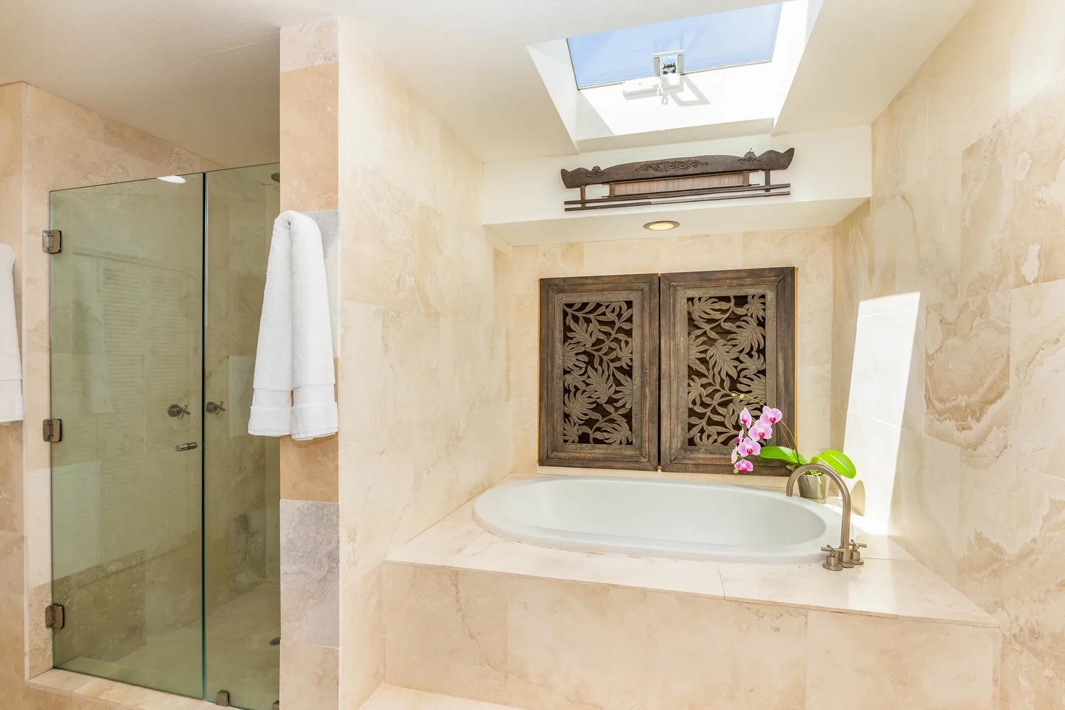 A marble bathroom with a glass shower, bathtub, and skylight.