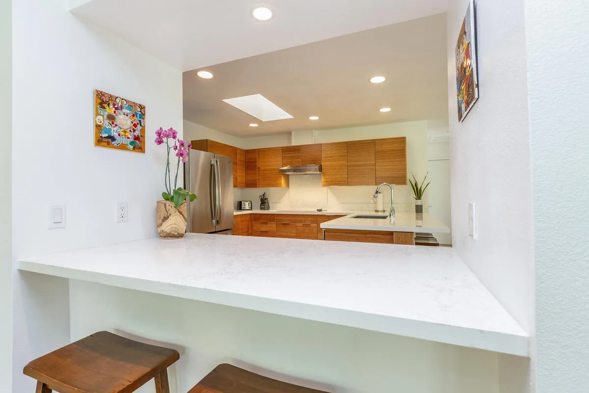 A bright kitchen with wooden cabinets and a broad white counter in the foreground.