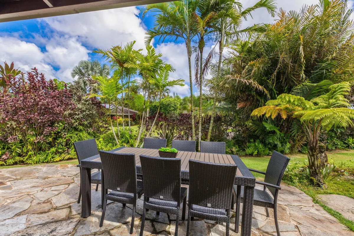 Un comedor al aire libre con asientos oscuros junto a un frondoso jardín tropical.