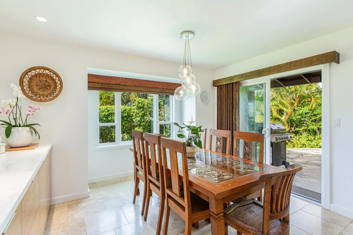 Un comedor luminoso con una mesa de madera junto a grandes ventanas y una puerta de vidrio abierta.