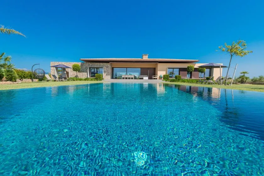 A modern house stands beside a large outdoor swimming pool under a clear blue sky.