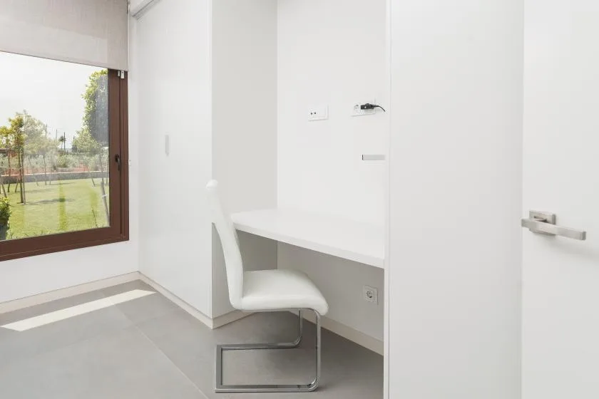 A small workspace with a white desk and chair beside a window.