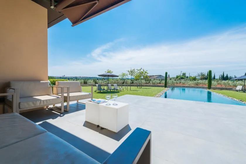 A patio with outdoor seating overlooks a swimming pool and landscaped grounds.