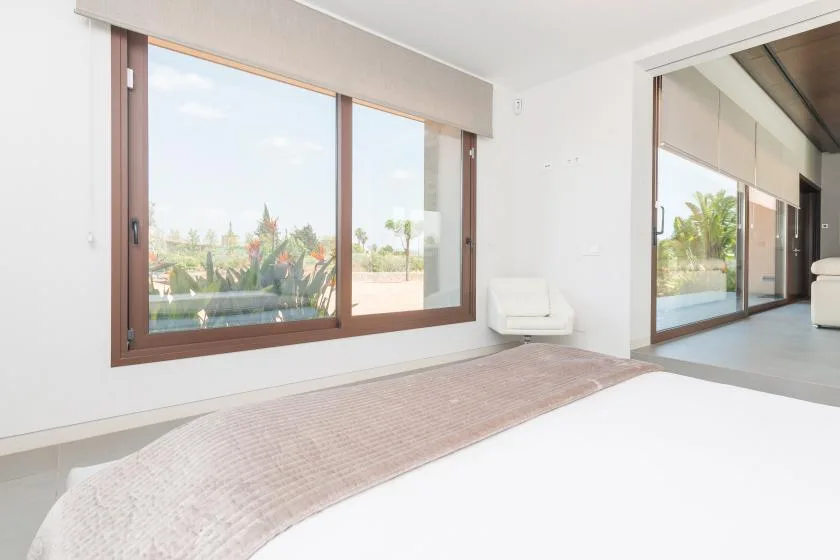 A bright bedroom with large windows overlooking greenery and a low upholstered bed.