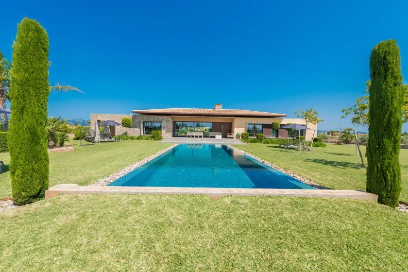 A swimming pool stretches across a landscaped lawn toward a modern single-story house.