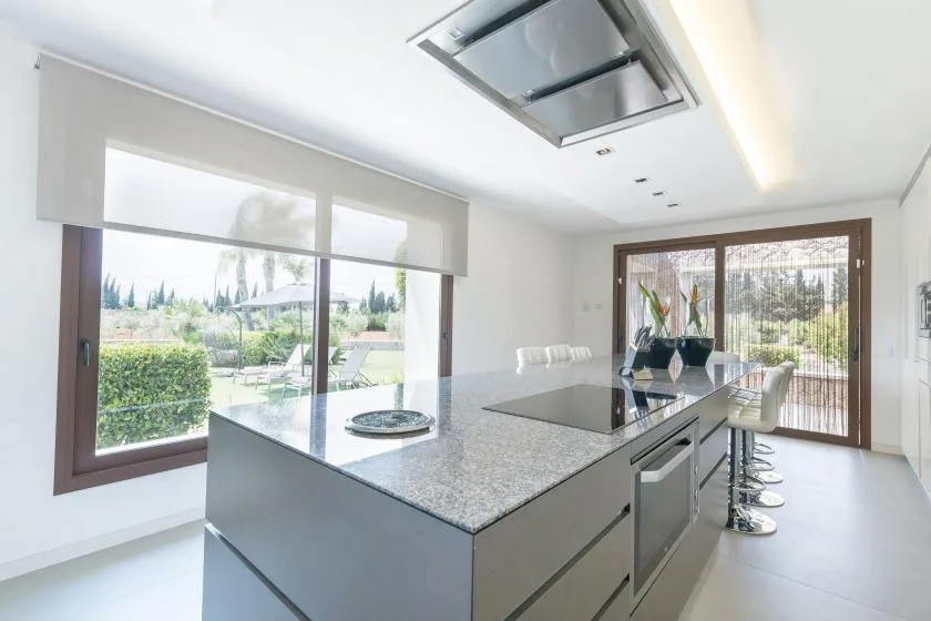 A modern kitchen with a large island and wide windows overlooking greenery.