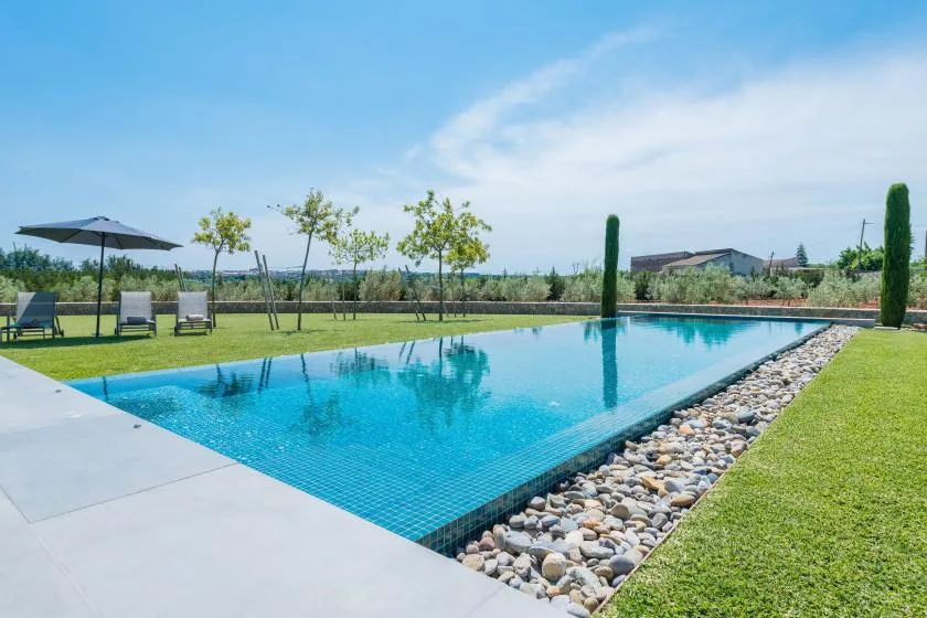 An outdoor swimming pool borders a green lawn and stone-lined edge.