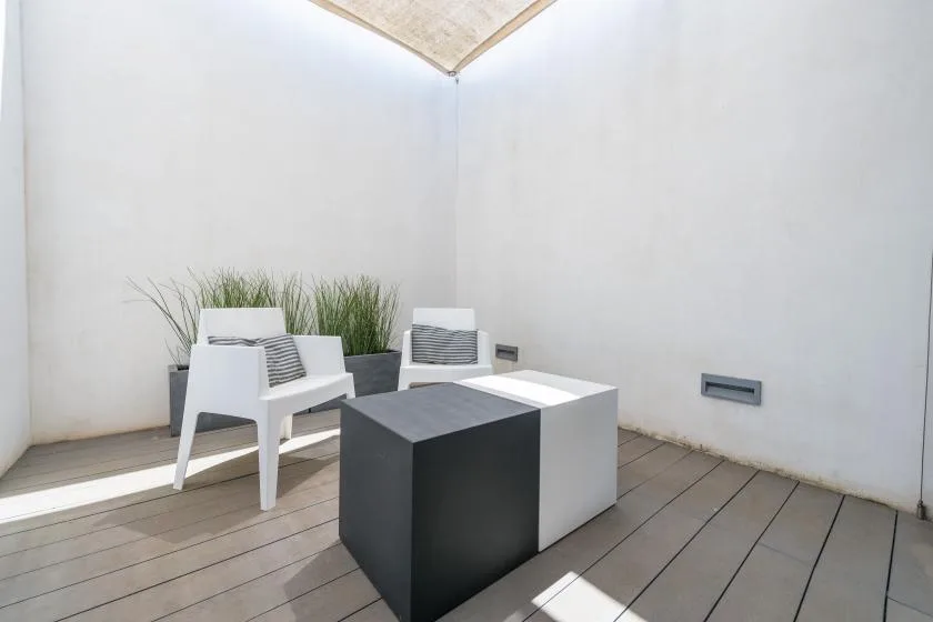 A bright patio seating area has two chairs beside a low geometric table and planters.