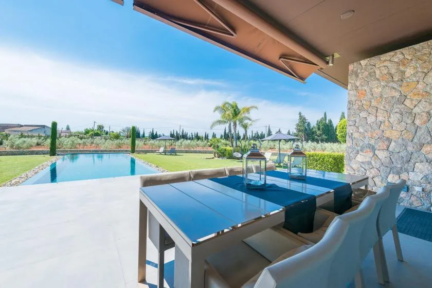 A covered outdoor dining area overlooks a swimming pool and landscaped garden.