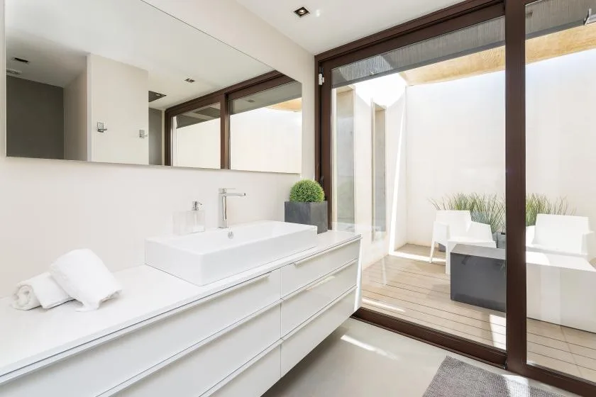 A bright bathroom with a long vanity and glass doors opening onto a patio.