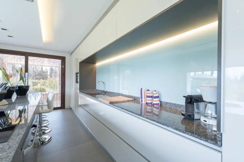 A modern kitchen with a long counter and dining table beside large windows.