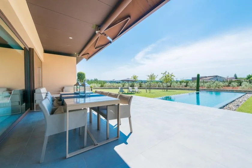 A covered patio with outdoor seating overlooks a swimming pool and landscaped grounds.