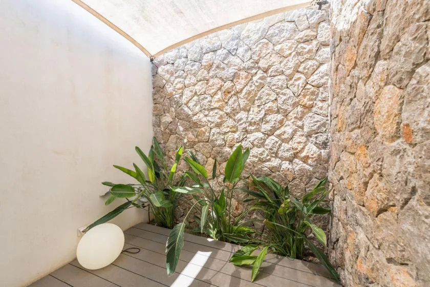 A small planted patio with stone walls and a light canopy overhead.