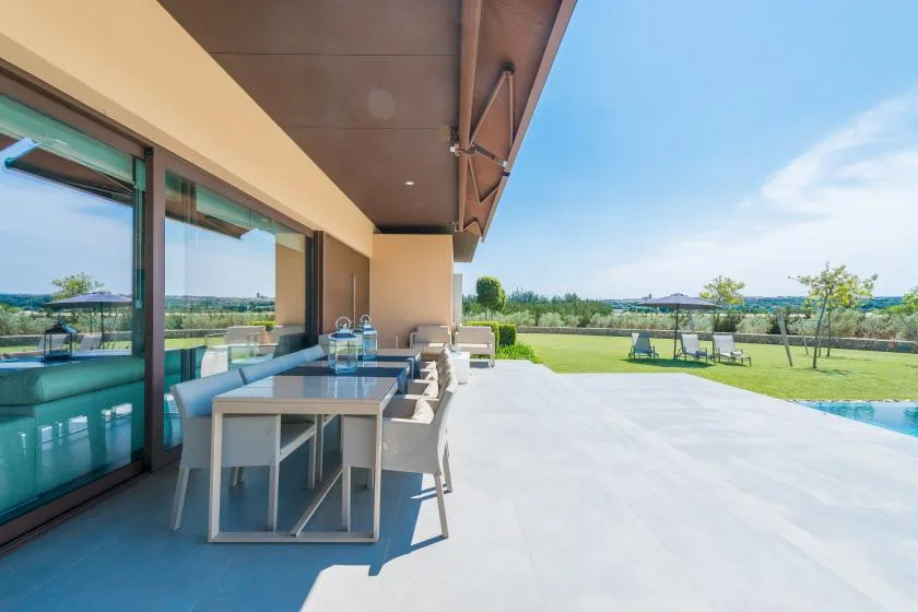 A covered patio with a dining table overlooks a lawn and swimming pool.