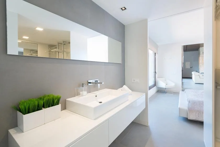 A bright bathroom with a long vanity, rectangular sink, and wide wall mirror.