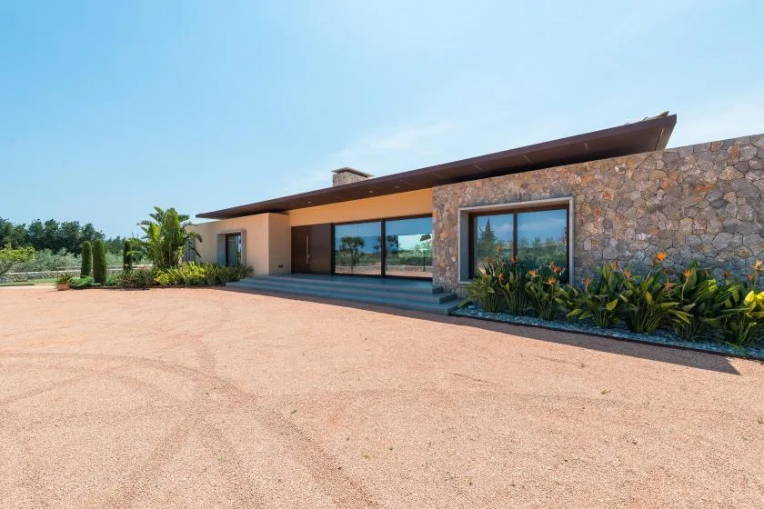 A modern single-story building with large windows opens onto a broad paved forecourt.