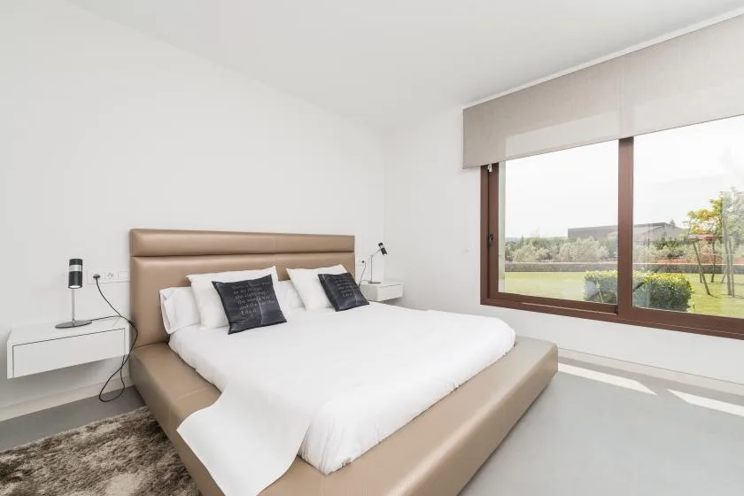 A bedroom with a bed beside a large window overlooking greenery.