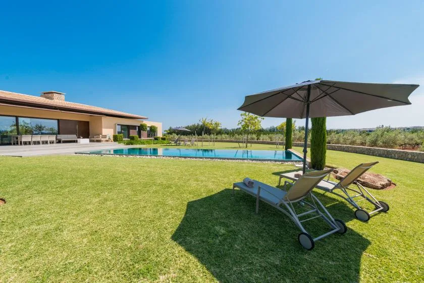 A landscaped outdoor pool area with lounge seating beneath a large umbrella.