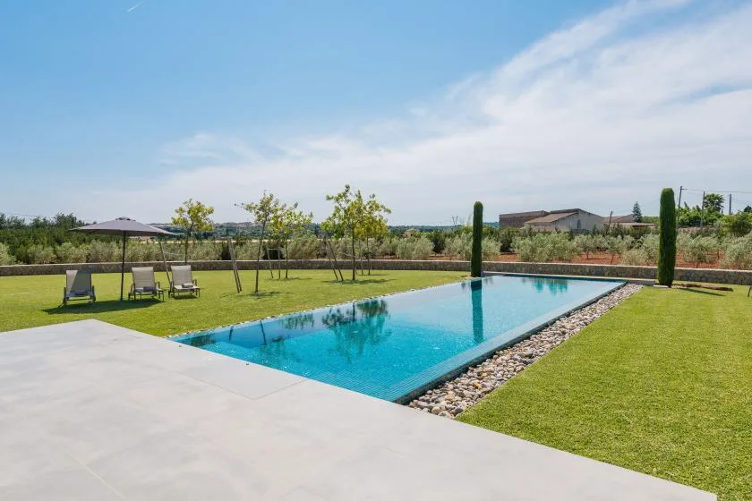 An outdoor swimming pool sits beside a broad lawn and paved patio.