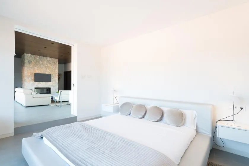 A bright bedroom with a large bed and an open doorway to a sitting area.