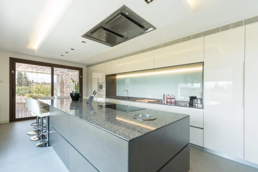 A modern kitchen with a large island and stools beside glass doors.