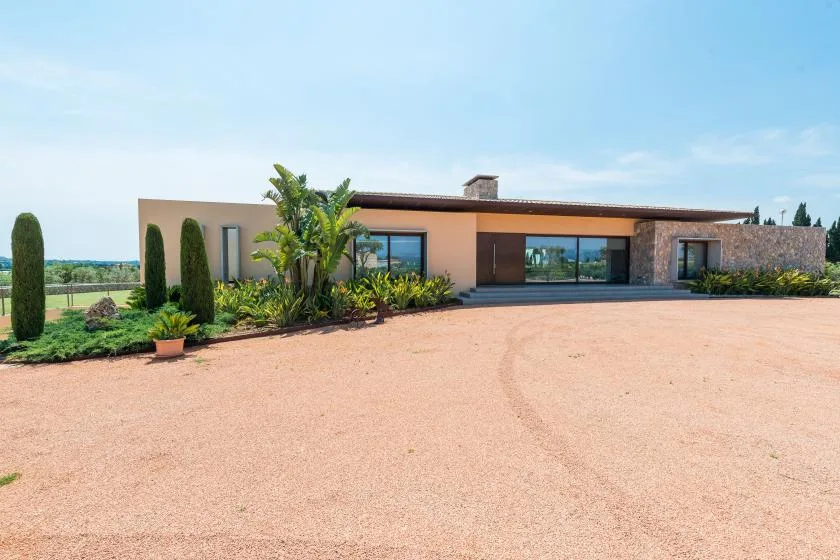 A modern single-story house sits beside a broad gravel driveway and landscaped garden.