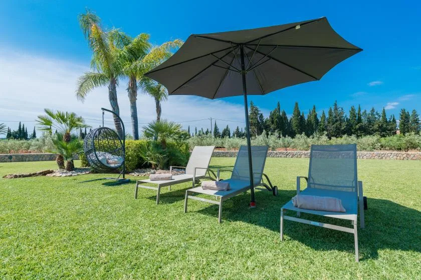 A sunny outdoor lawn seating area with loungers beneath a large umbrella.