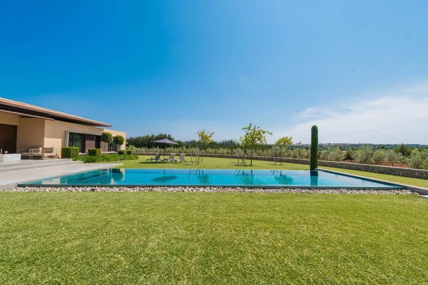 A swimming pool beside a modern house, with lawn and open countryside beyond.