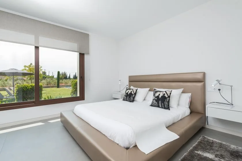 A bright bedroom with a large bed and a wide window overlooking greenery.