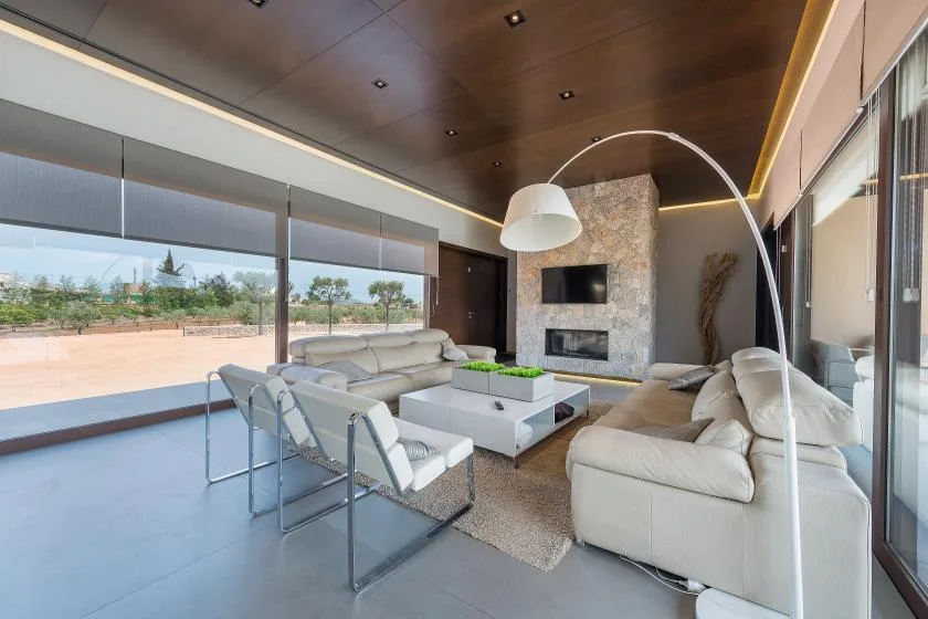 A modern living room with light seating, a coffee table, and large windows.