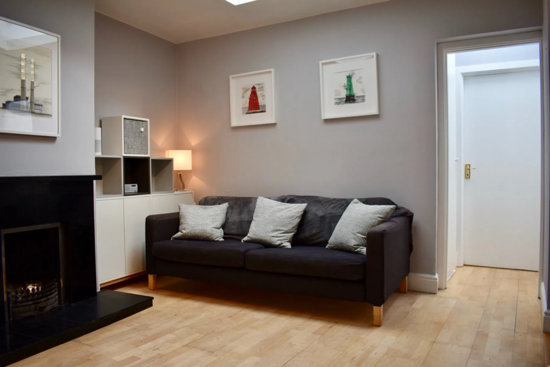 A living room with a dark sofa, framed pictures, and a fireplace.