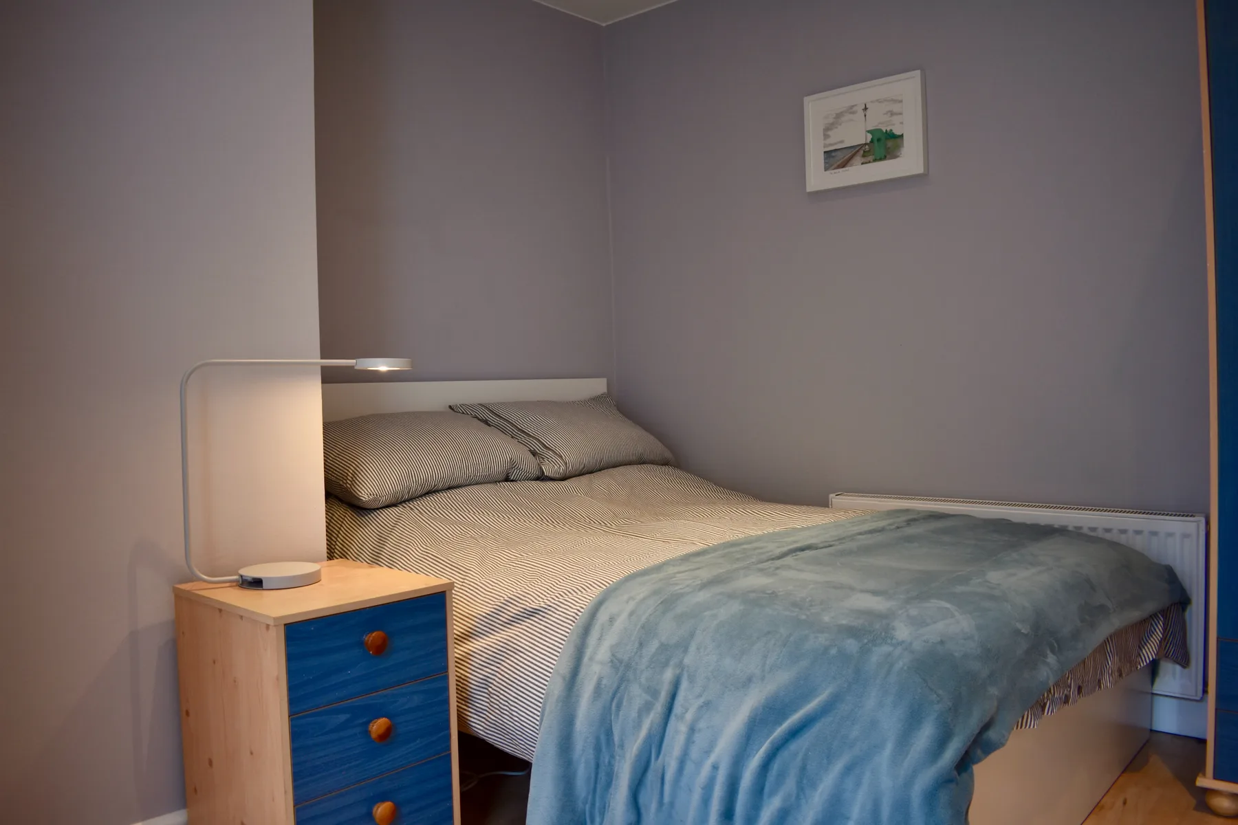 A bedroom with a bed covered by a blue blanket and a bedside table.