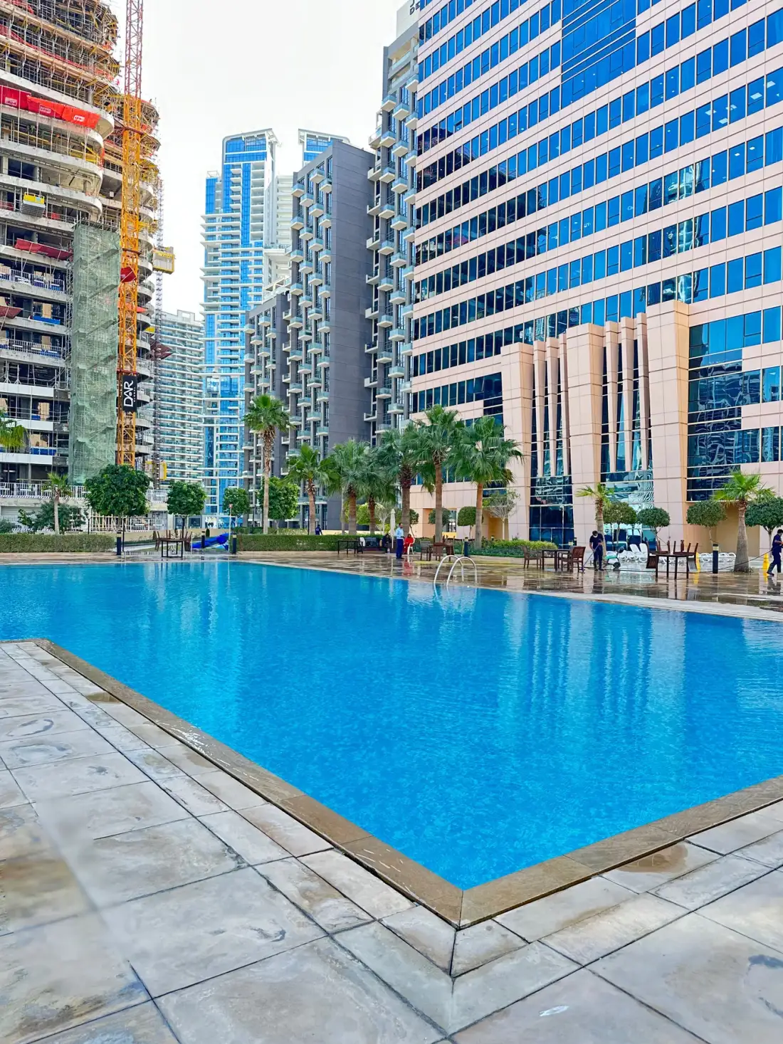 Una piscina está rodeada de edificios modernos de gran altura y palmeras.