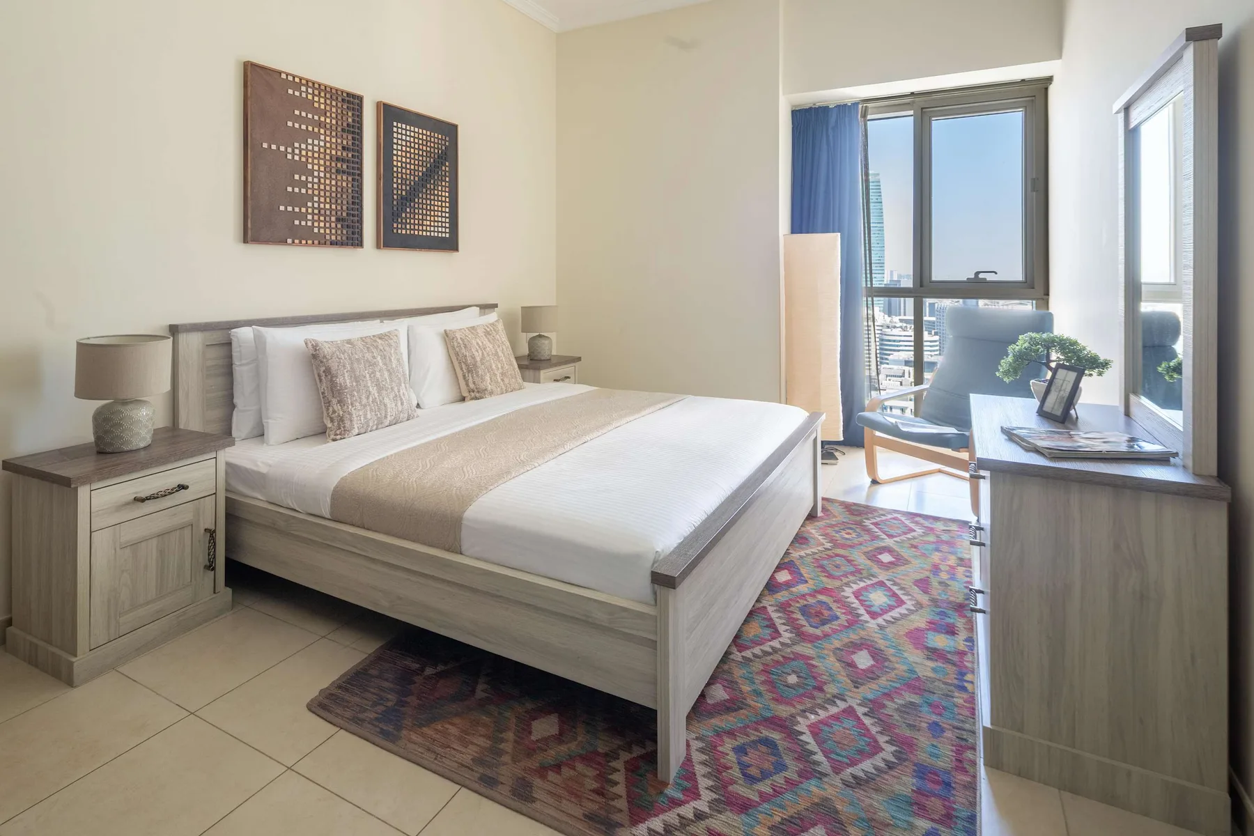 Un dormitorio luminoso con una cama bien tendida y ventanas grandes.