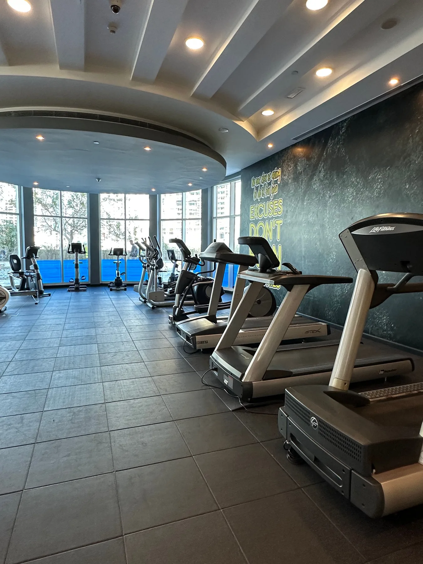Un gimnasio con cintas de correr y equipos de ejercicio junto a ventanales.