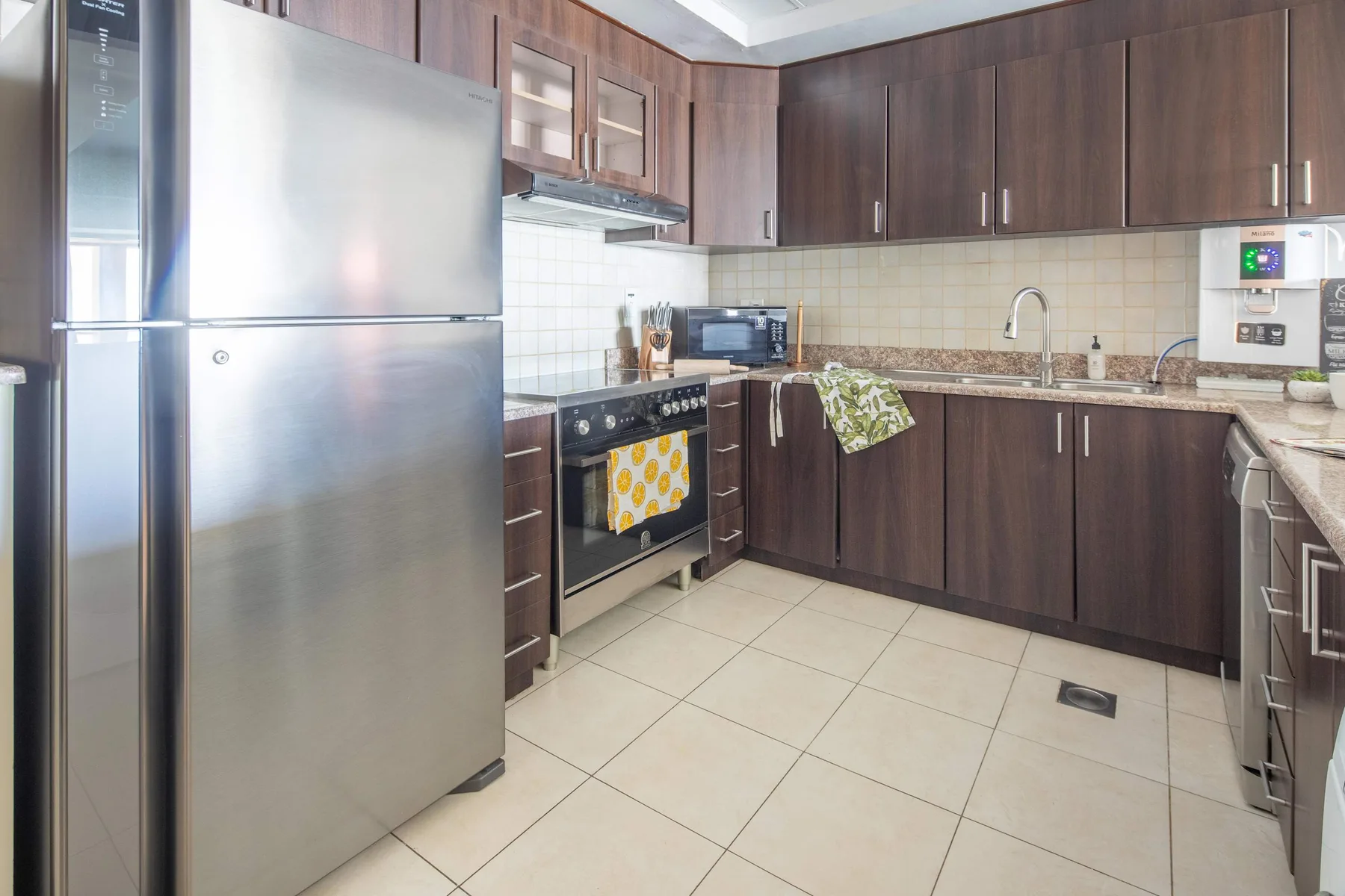 Una cocina con gabinetes oscuros, un refrigerador y piso de baldosas.