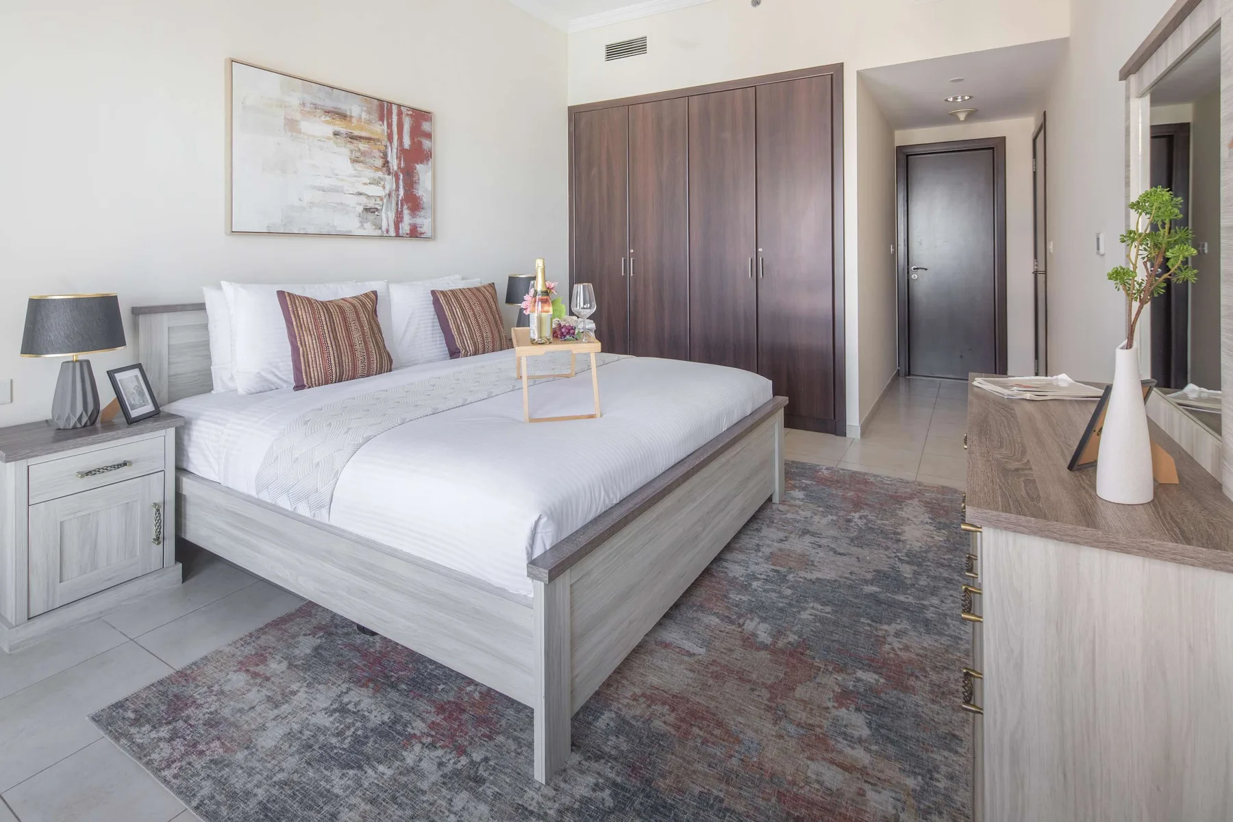 Un dormitorio luminoso con una cama tendida y un armario de madera oscura.