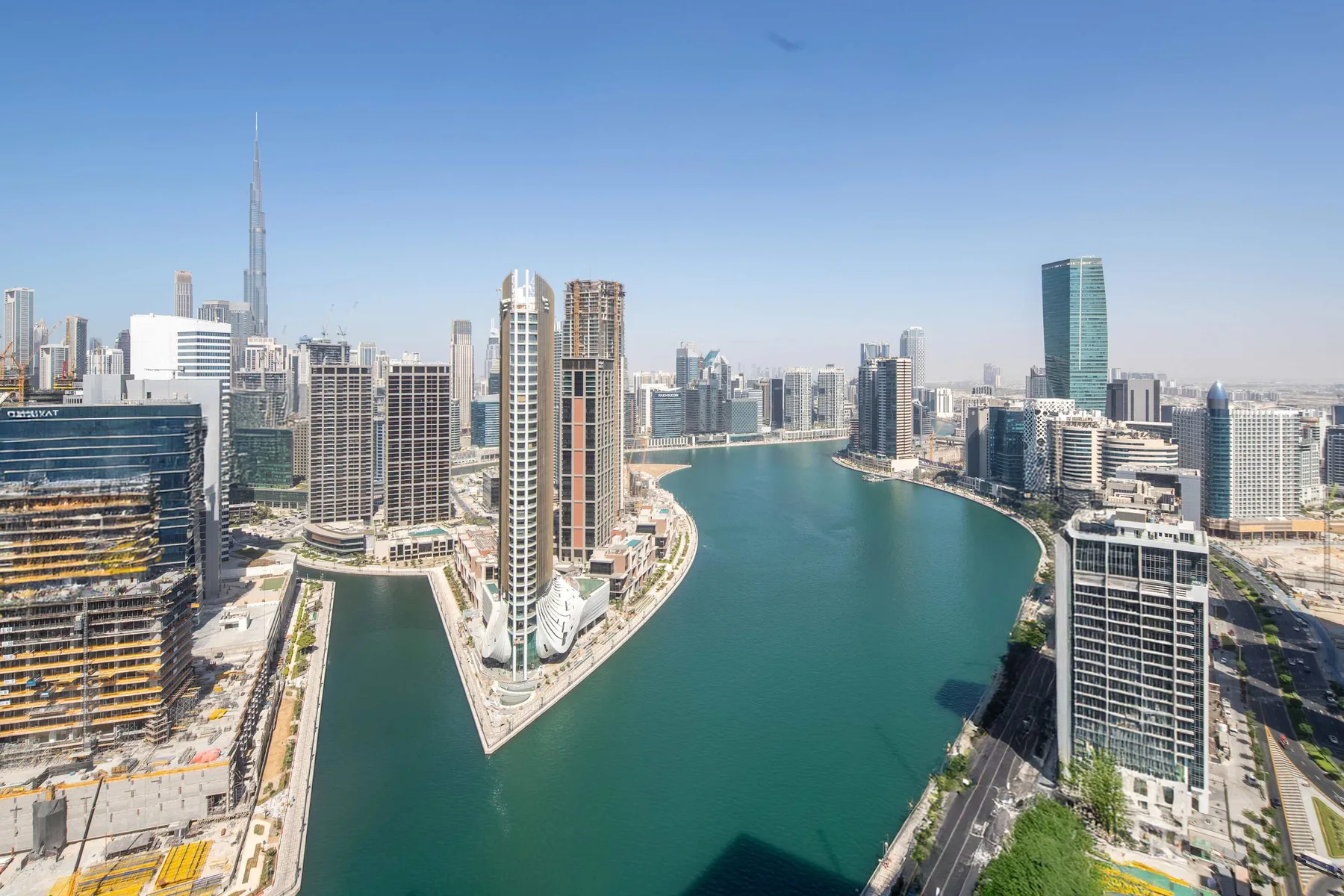 Vista aérea del horizonte de una ciudad junto a un canal curvo bajo un cielo despejado.