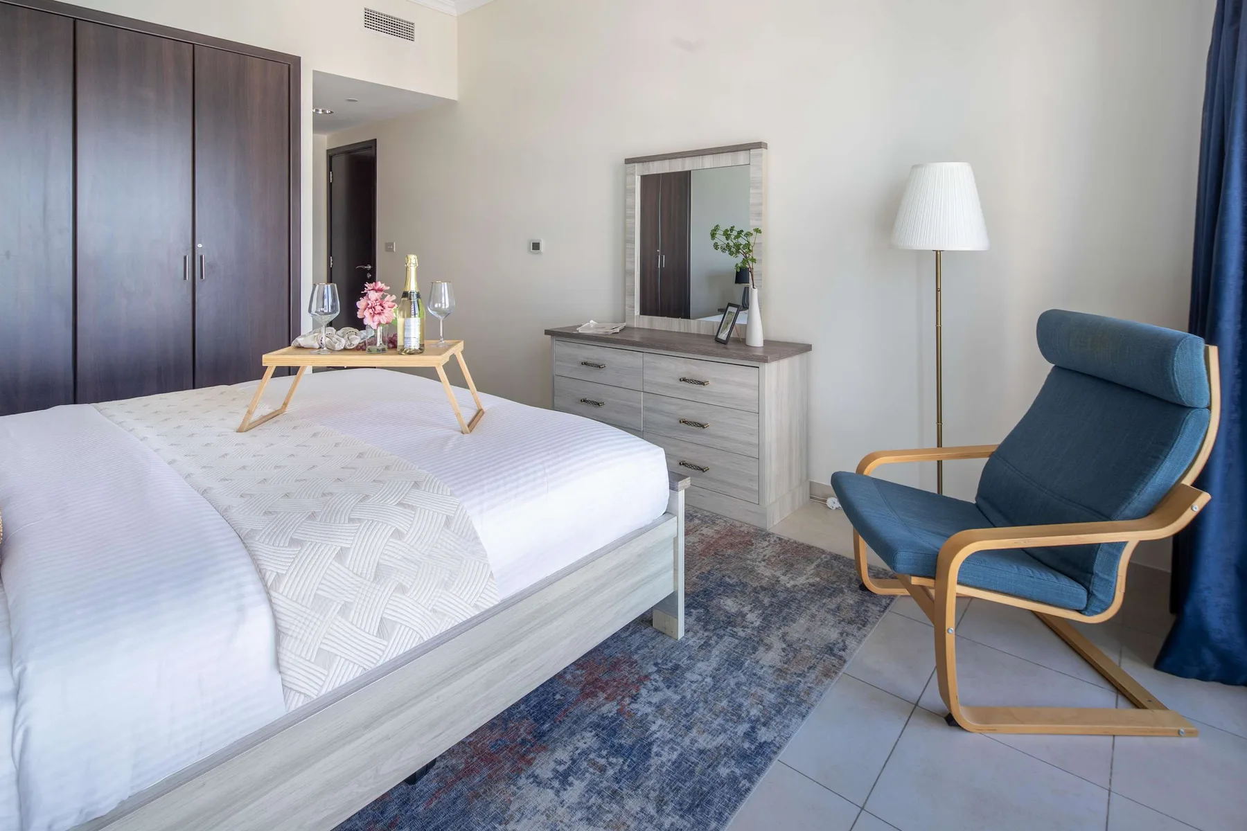 Un dormitorio luminoso con una cama blanca y un sillón azul.