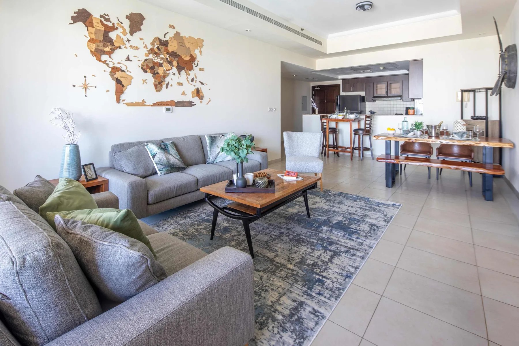 Una sala luminosa con asientos grises, una mesa de centro y una cocina abierta.