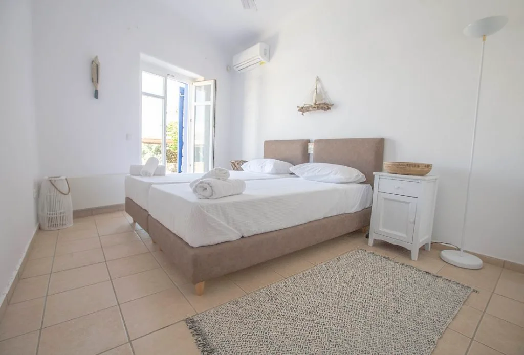 A bright bedroom with a bed, bedside cabinet, and open balcony doors.