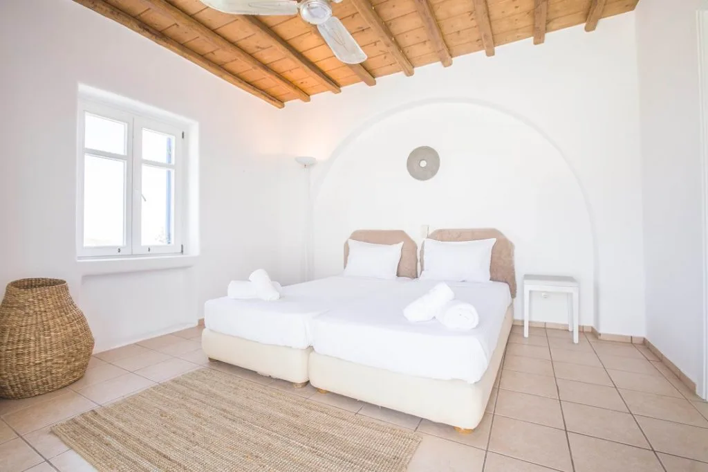 A bright bedroom with a white bed beneath a wooden ceiling.