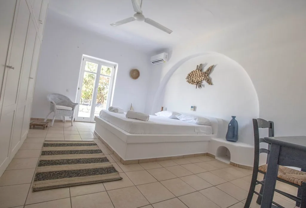 A bright bedroom with a raised bed, a small seating area, and a ceiling fan.