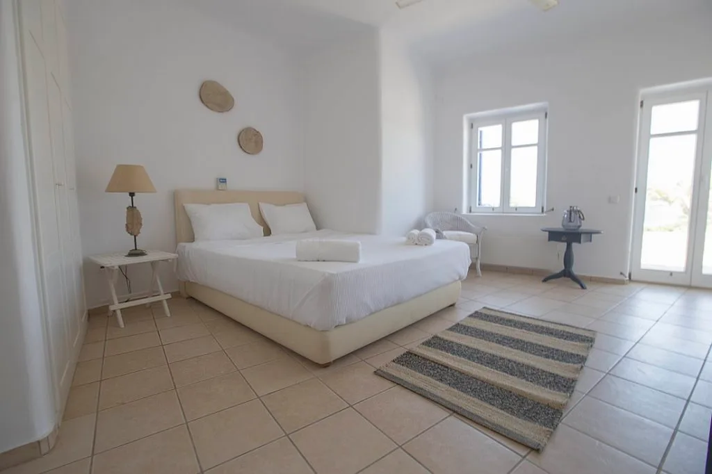A bright bedroom with a large bed and a small table beside the window.