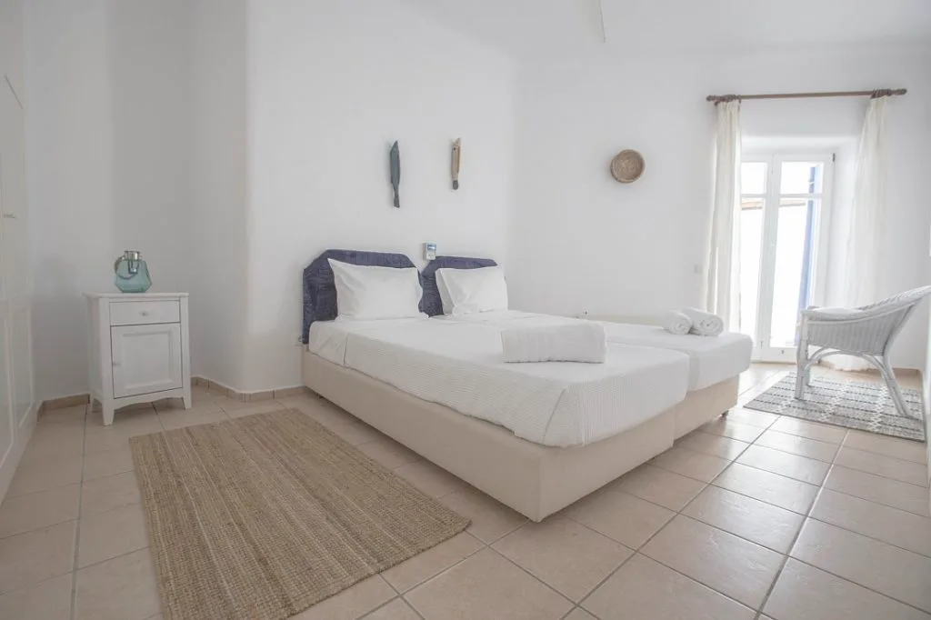 A bright bedroom with two beds and a woven rug.