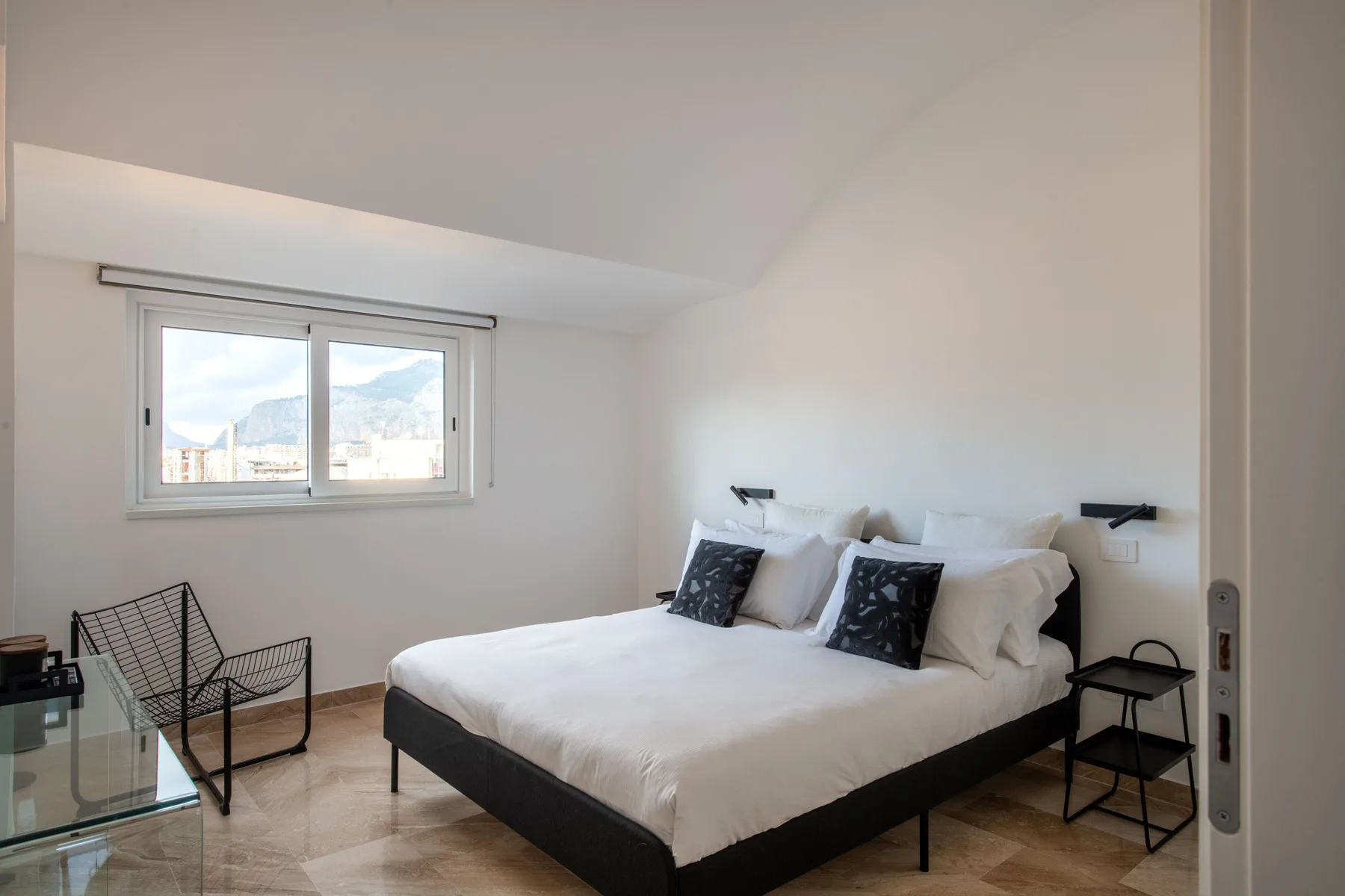 A bright bedroom with a double bed and a window overlooking the mountains.