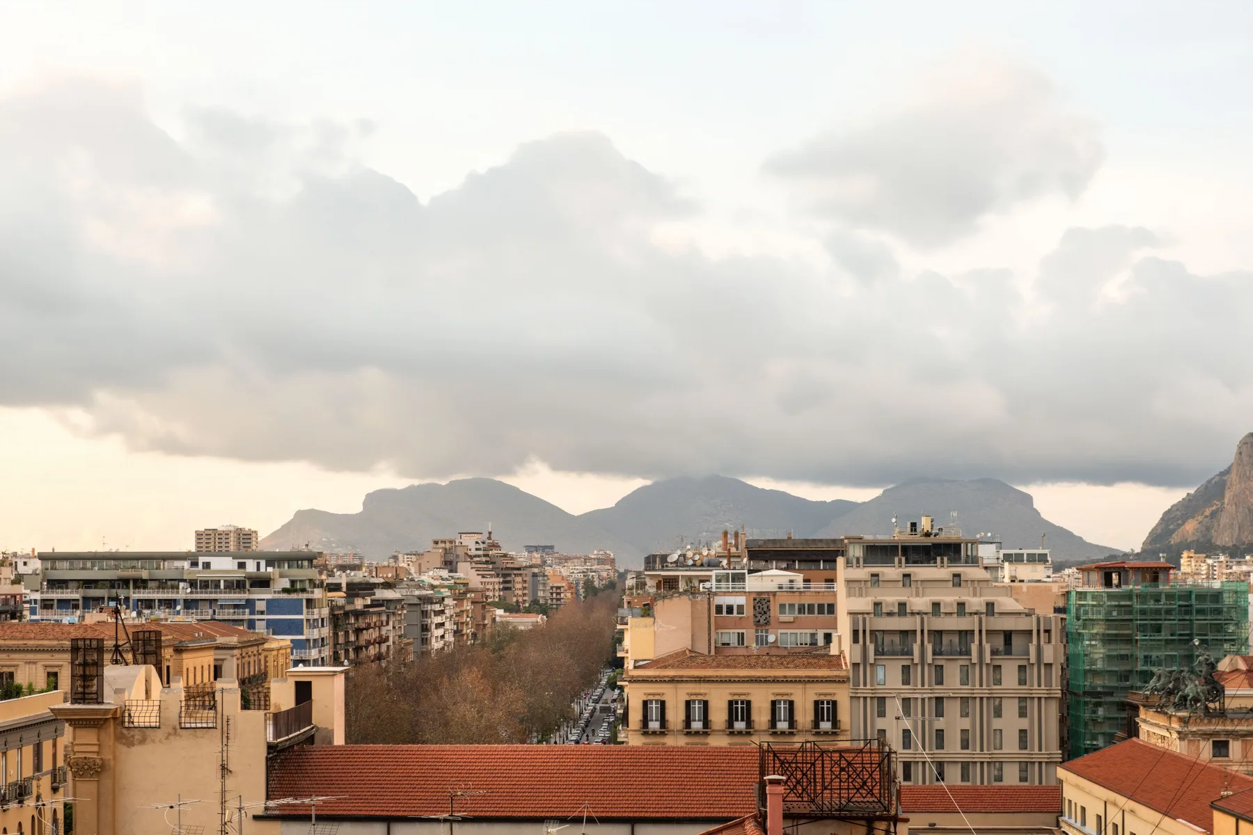 Un perfil urbano con edificios agrupados bajo un cielo nublado y montañas lejanas.